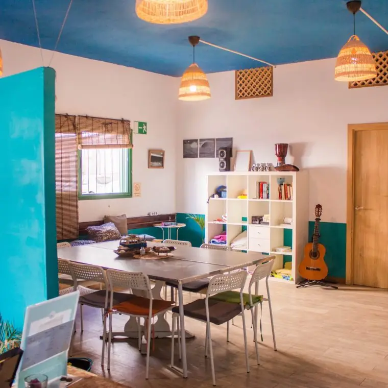 Sala común del hostel Sala común de Single Fin Surf Hostel con mesa grande, estantería y guitarra