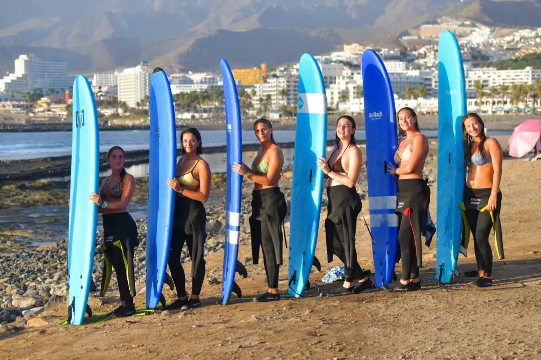 La familia Single Fin en Playa de Las Américas Alumnas de Single Fin posando con sus tablas de surf en Playa de Las Américas, Tenerife, con las montañas al fondo
