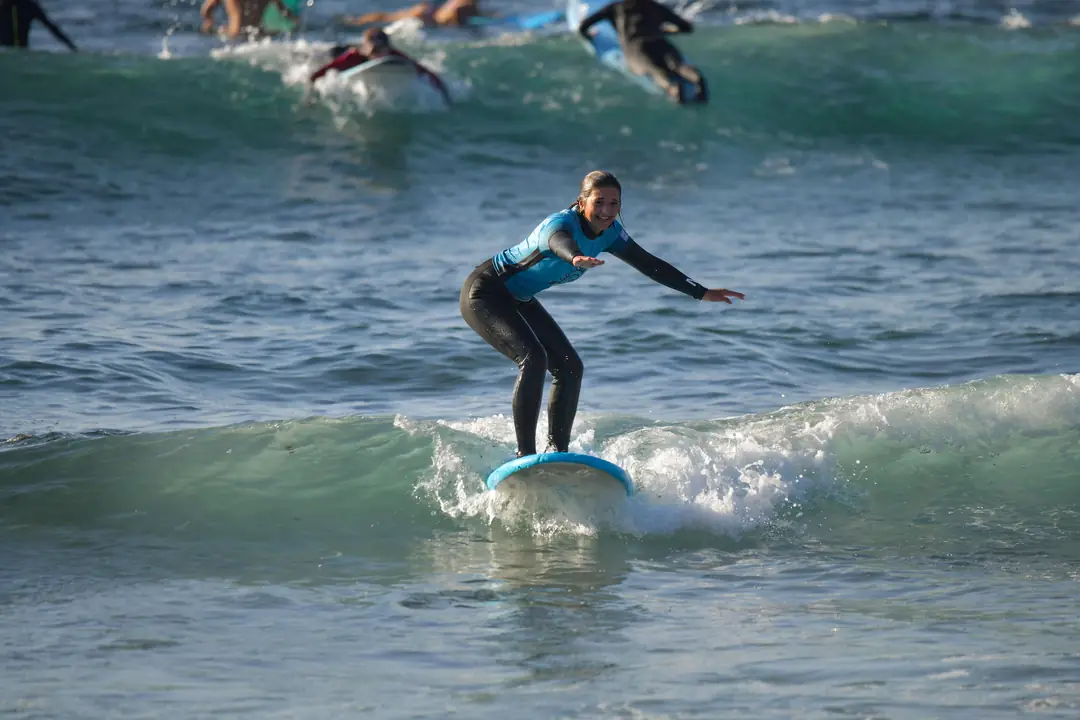 Clase de surf en Playa de Las Américas Alumna de pie sobre la tabla cogiendo una ola durante una clase de surf en Playa de Las Américas